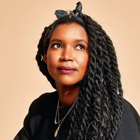 Tamara Shogaolu, a black woman with long black thick two-strand twist braids. She is confidently gazing above and to the right of the camera. She is wearing a black hair-scarf tied in a bow on the top of her head, a black shirt, and two thin golden necklaces with small charms, as well as a thin nose ring in her (personal) right nostril. She is positioned in front of a beige background.