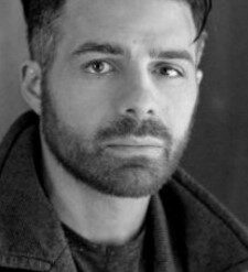 Photograph in grayscale of a man with a beard and peacoat.