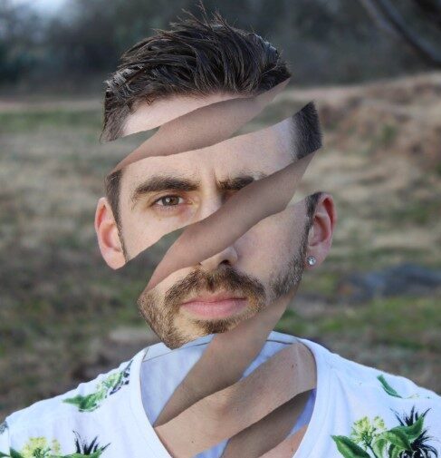 A white man in his mid 30s with medium brown hair, a short beard, and a simple stud jewel earring. He is outside in nature, with a blurry tree in the background. He has heavily photoshopped the photo to create the surreal illusion that his head is hollow, and his face is being unraveled in a radial fashion, like one might peel an orange. This might sound grotesque but it’s not, just weird and cool looking lol.