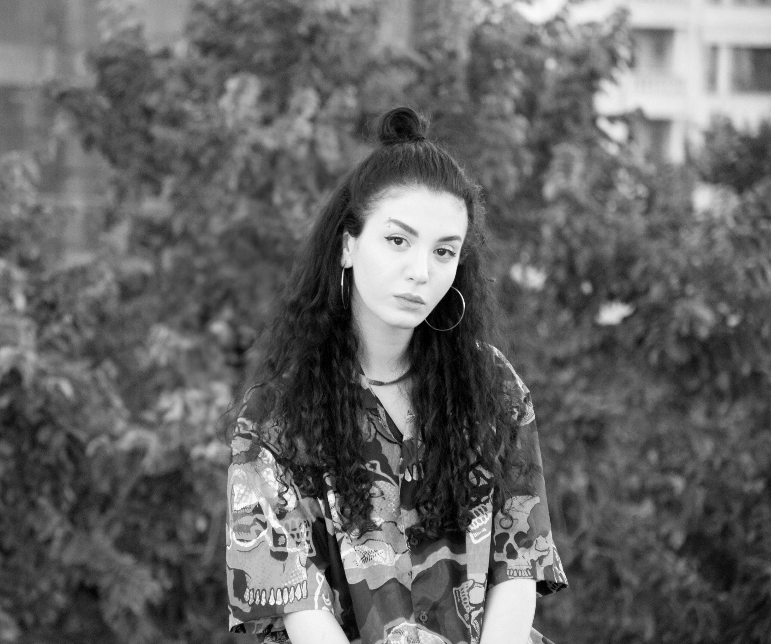 Ghazal Majidi, a woman with light skin and dark long curly hair, looking into the camera with mouth closed. She is wearing a patterned short sleeve. The photo is in black and white.