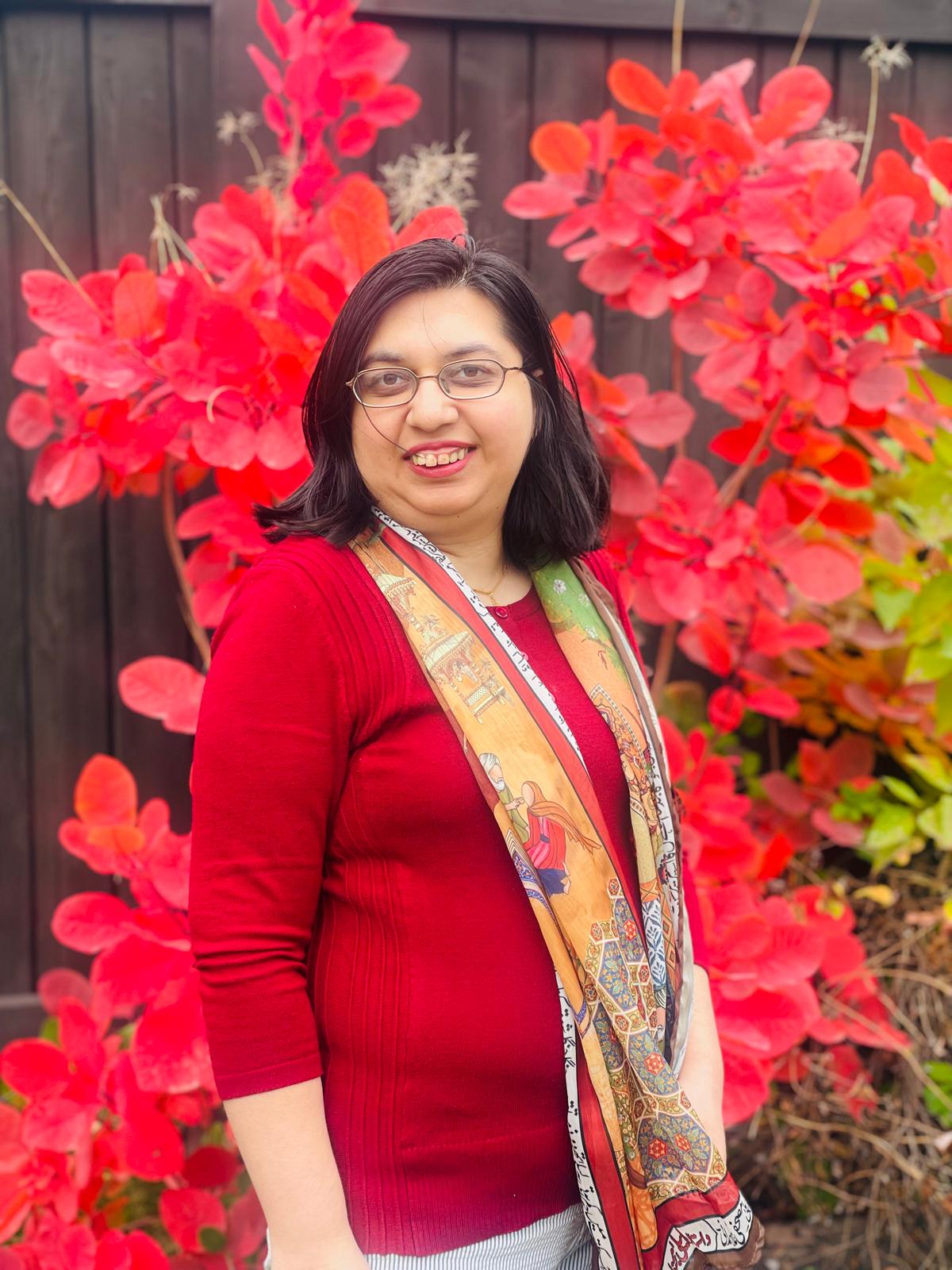 Hunyah Irfan ,a Pakistani person with light skin ,brown eyes and black hair standing beside the flowers.